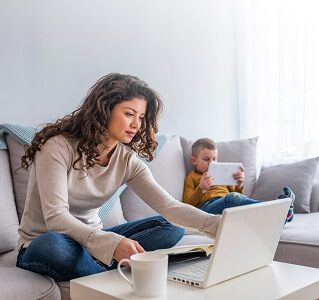 Woman using a laptop sat on the sofa with her child